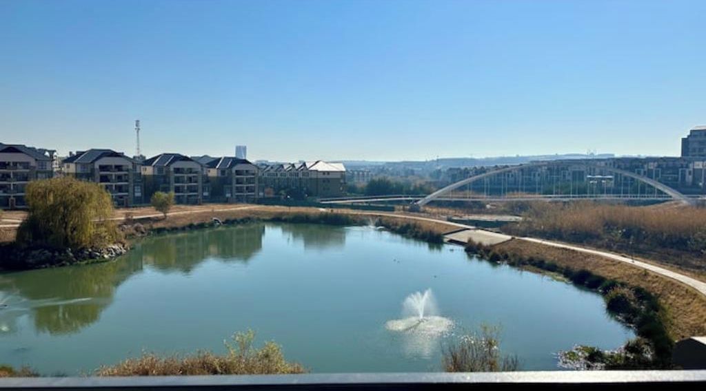 A residential area with a pond, a bridge, and apartment buildings.