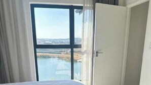 Habitación de hotel con cama, vista a un cuerpo de agua y puerta que da a otra habitación.