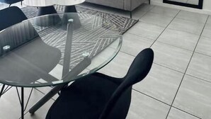 Una sala de estar moderna con un sofá gris, sillas negras y azules, una mesa de centro de vidrio y un cuadro abstracto grande en la pared.