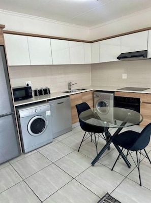 A compact kitchen with a washing machine, a dishwasher, a sink, and a dining table with chairs.