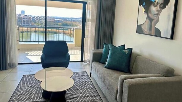 Un moderno salón con un sofá, una mesa de centro redonda y vistas a un balcón con barandilla.