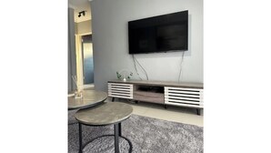 Una sala de estar moderna con un televisor de pantalla plana montado en la pared, un mueble de madera debajo y una mesa de centro redonda sobre una alfombra gris.