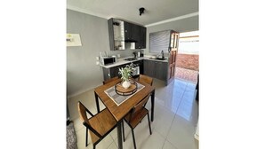 Una cocina moderna con muebles oscuros, una isla central y una zona de comedor con una mesa y sillas de madera.