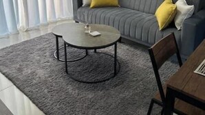 Una sala de estar con un sofá gris, una mesa de centro redonda y una mesa de comedor con sillas.