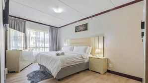 A bedroom with a bed, bedside tables, a dresser, and a window with curtains. - Gem in Fourways Modern 2-Bed Apartment (Randburg)
