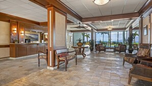A spacious lobby with a reception desk, seating area, and large windows offering a view of the ocean. - Oceanfront Maui Escape! Panoramic Views, Pool, Hot Tub & Steps to Beach (Lahaina)