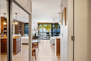 A modern kitchen with wooden cabinets, a dining area with a table and chairs, and a balcony with a view of palm trees.