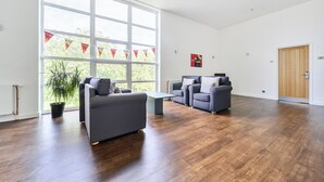 Ein geräumiger Raum mit großem Fenster, zwei Sofas, einem kleinen Tisch und einer Holztür.