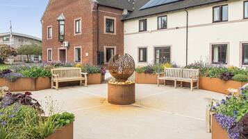 A courtyard with two wooden benches, a decorative spherical sculpture, and flower beds.
