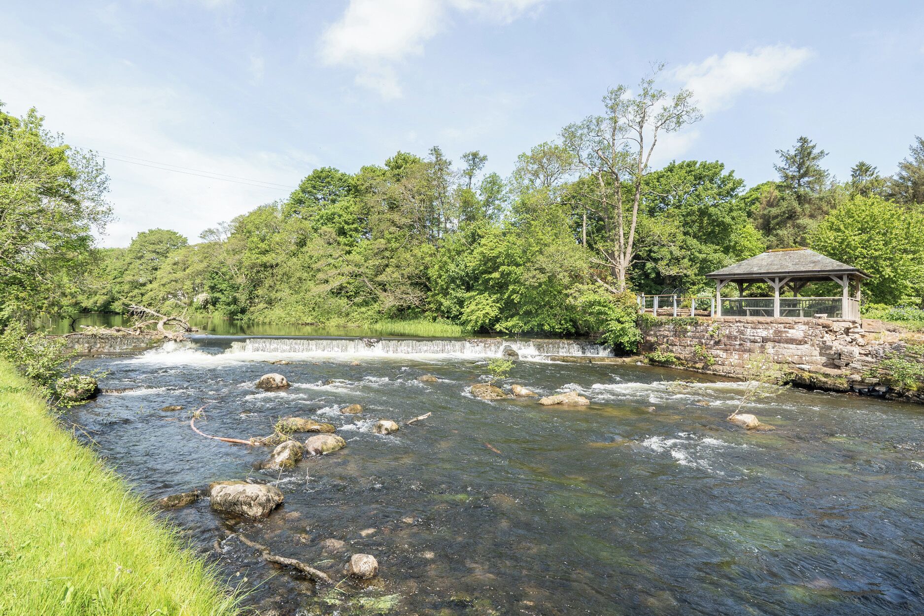 A river with rocks, a gazebo, and lush greenery.