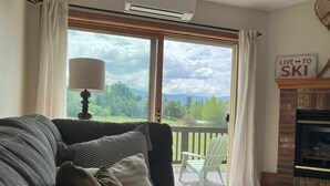 A living room with a sofa, a lamp, a fireplace, and a view of a green landscape through a sliding glass door.