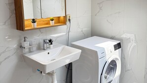 A modern bathroom with a built-in sink, a mirror, and a front-loading washing machine. - Riverside Apartment 15 (Hlavní město Praha)
