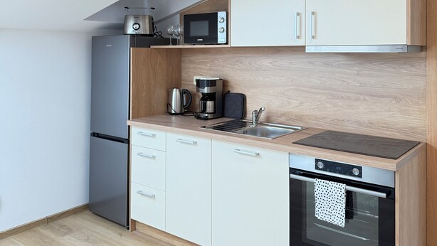A modern kitchen with white cabinets, a built-in oven, a microwave, a coffee maker, and a sink. - Riverside Apartment 15 (Hlavní město Praha)
