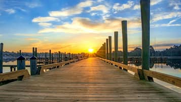 A wooden pier extending into calm water with a sunset in the background.
