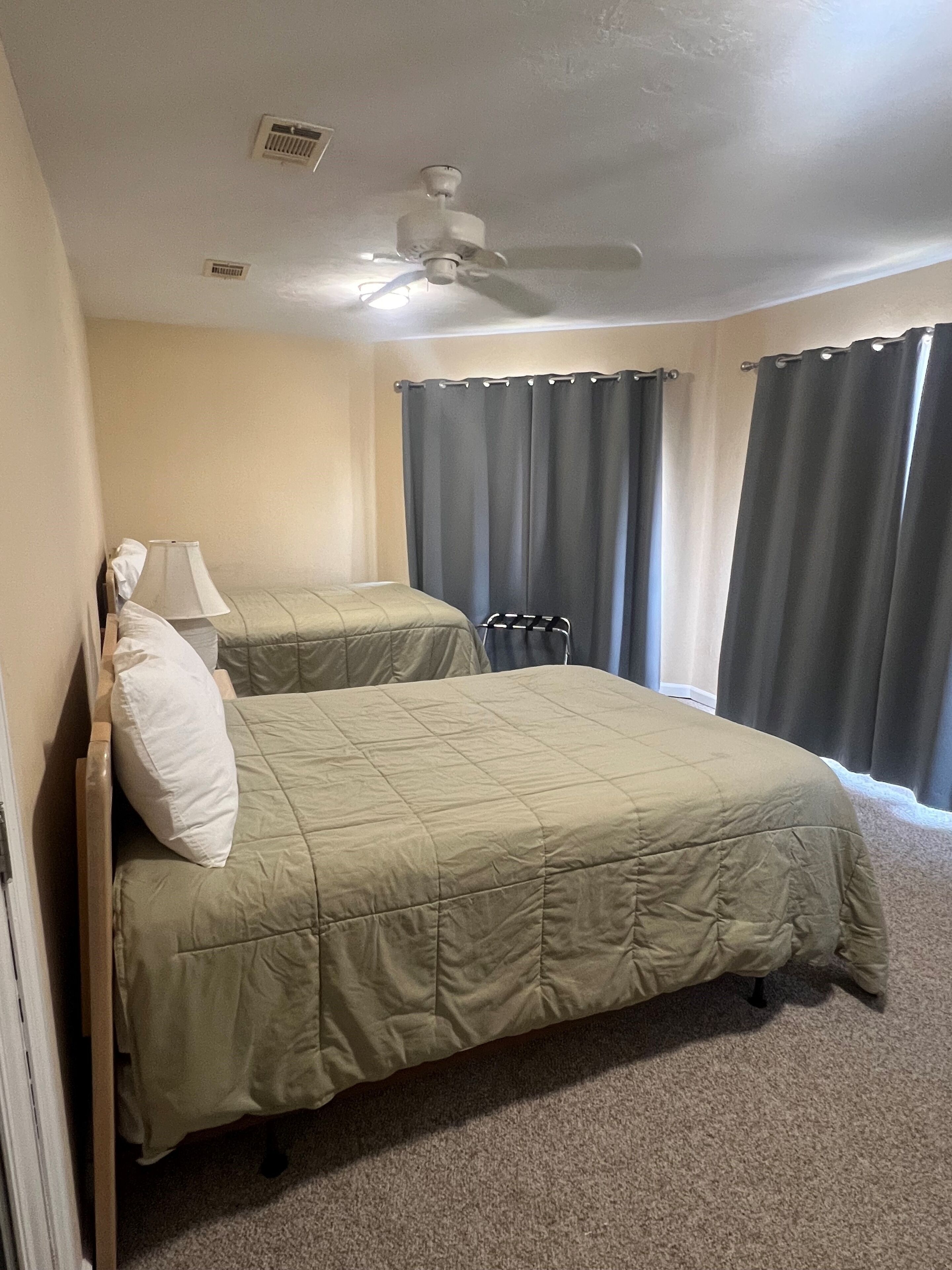 A bedroom with a bed, a window with blinds, a ceiling fan, and a small window vent.