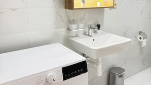 A modern bathroom with a white washing machine, a sink, and a mirror with a wooden frame. - Riverside Apartment 16 (Hlavní město Praha)