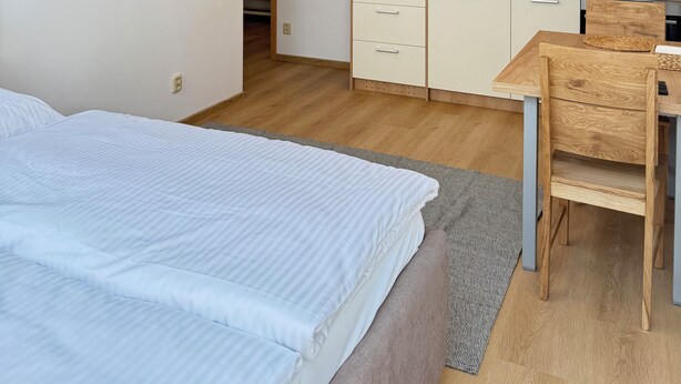 A modern bedroom with a bed, a wooden dining table, and a kitchenette with cabinets and a microwave. - Riverside Apartment 16 (Hlavní město Praha)