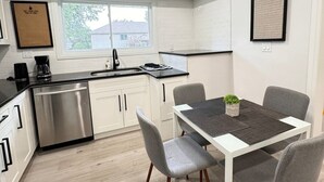 A modern kitchen with white cabinets, a stainless steel dishwasher, and a black countertop. There is a window with a view of the outside, and a framed quote on the wall.