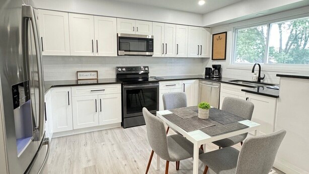A modern kitchen with white cabinets, stainless steel appliances, and a dining area with a table and chairs.