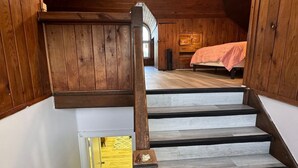 A wooden staircase with a handrail leading to a bedroom with a bed and a window.
