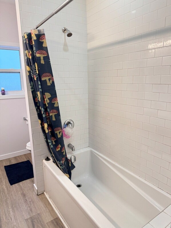 A bathroom with a white tiled shower, a bathtub, and a window with a view.