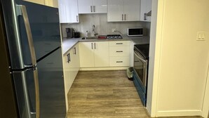 A compact kitchen with white cabinets, a stainless steel refrigerator, a microwave, and a stove.