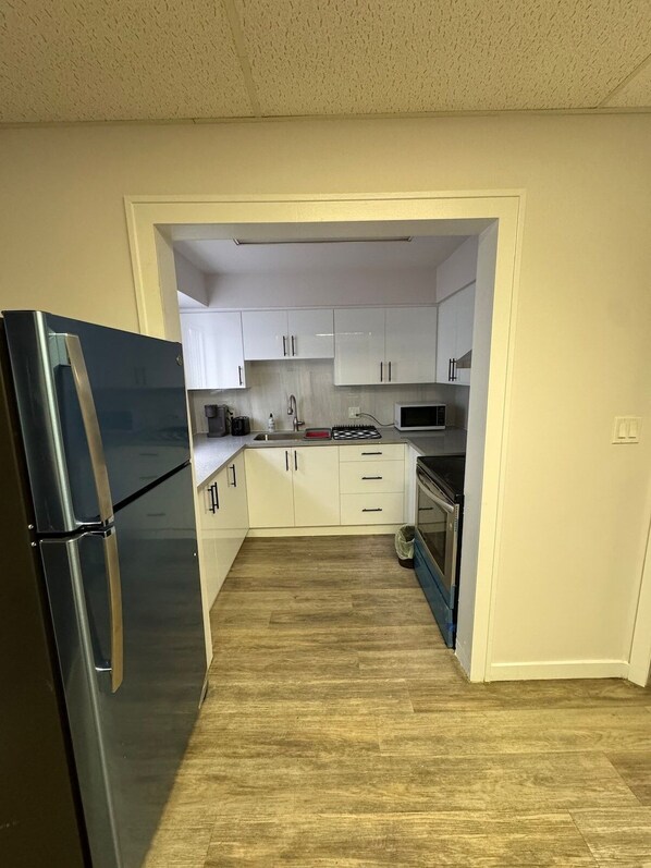 A compact kitchen with white cabinets, a stainless steel refrigerator, a microwave, and a stove.