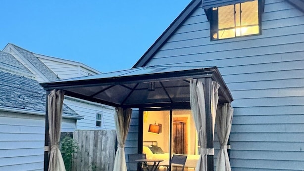 Un patio couvert avec une table et des chaises, une terrasse en bois et une maison en arrière-plan.