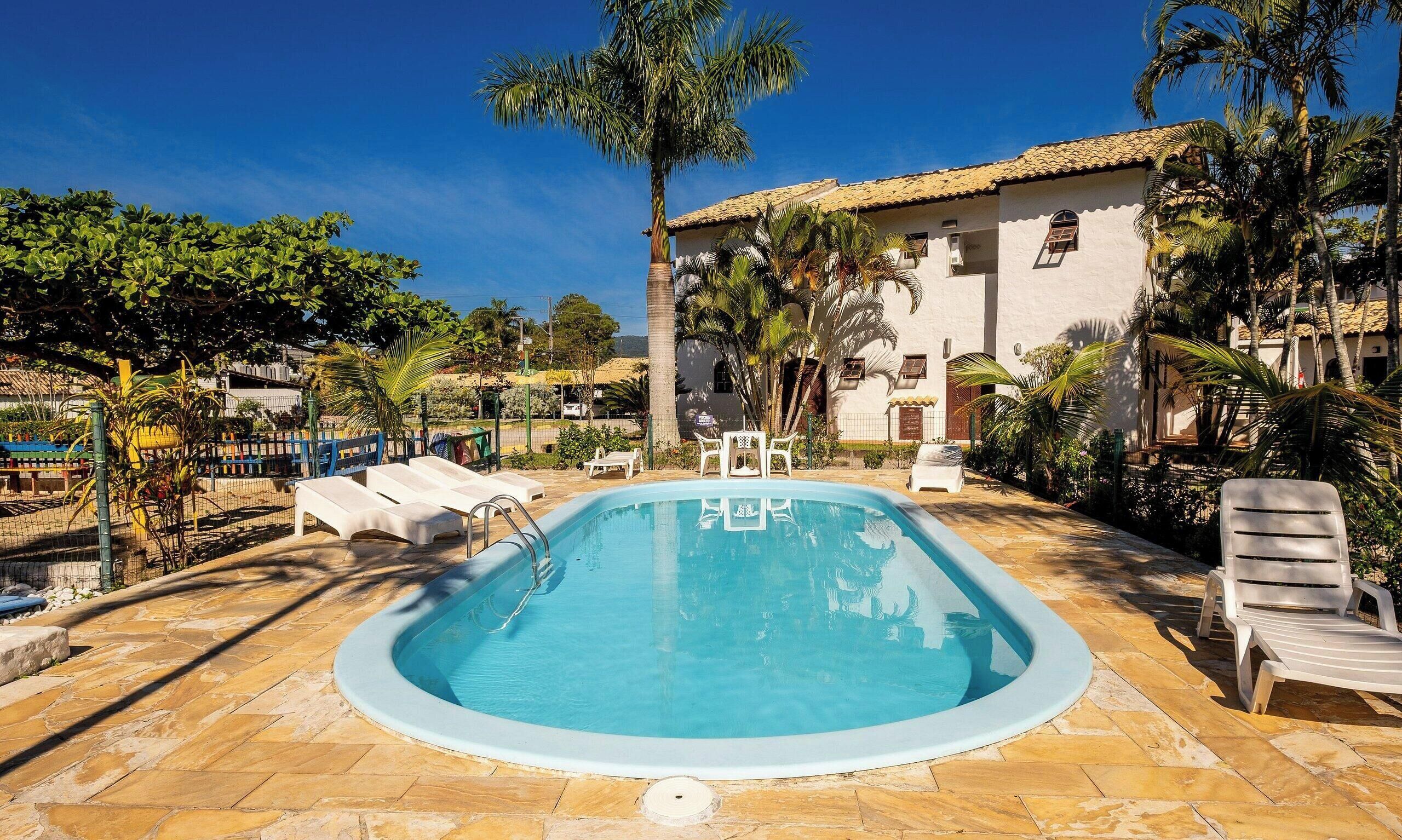 A swimming pool with lounge chairs, surrounded by palm trees and a building with a tiled roof.