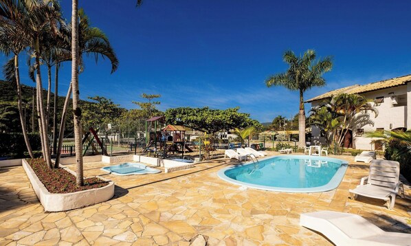A pool area with multiple pools, lounge chairs, and palm trees. - Encantador Apto Beira-mar Floripa Rpb037 (Florianópolis)