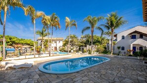 A swimming pool surrounded by stone tiles, palm trees, and a white building with blue accents. - Encantador Apto Beira-mar Floripa Rpb037 (Florianópolis)