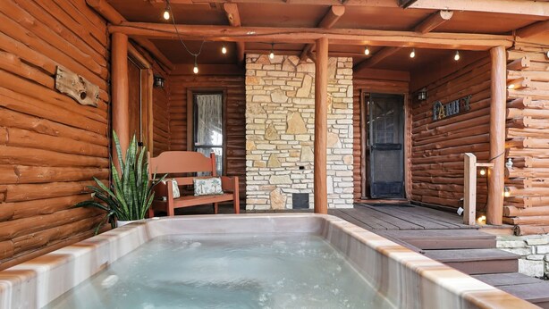 Una cabaña de madera con pared de piedra, un jacuzzi y un banco de madera.