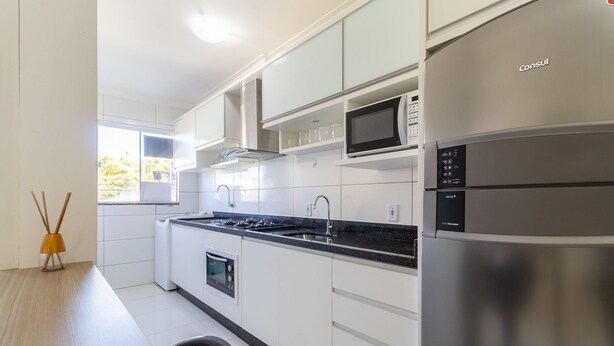 A modern kitchen with white cabinets, a stainless steel refrigerator, a microwave, and a built-in oven.
