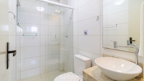 A modern bathroom with a glass-enclosed shower, a white toilet, and a large oval sink with a mirror above it.