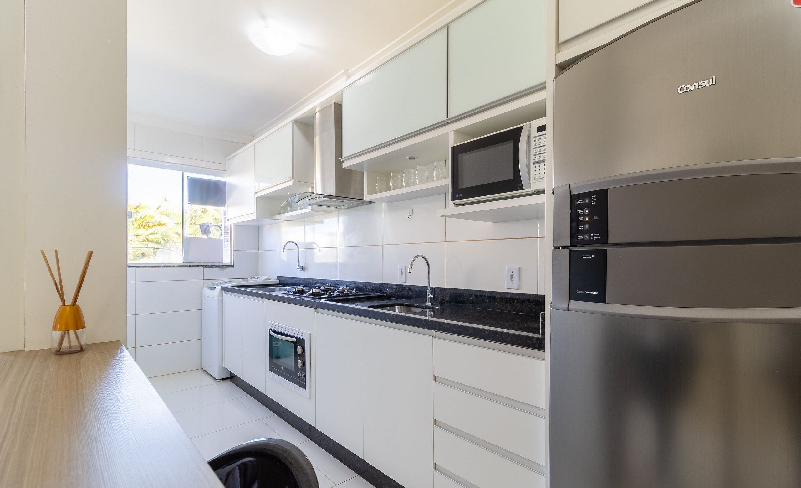 Una cocina moderna con armarios blancos, un refrigerador de acero inoxidable, un microondas y un horno empotrado.