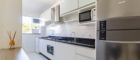 Una cocina moderna con armarios blancos, un refrigerador de acero inoxidable, un microondas y un horno empotrado.