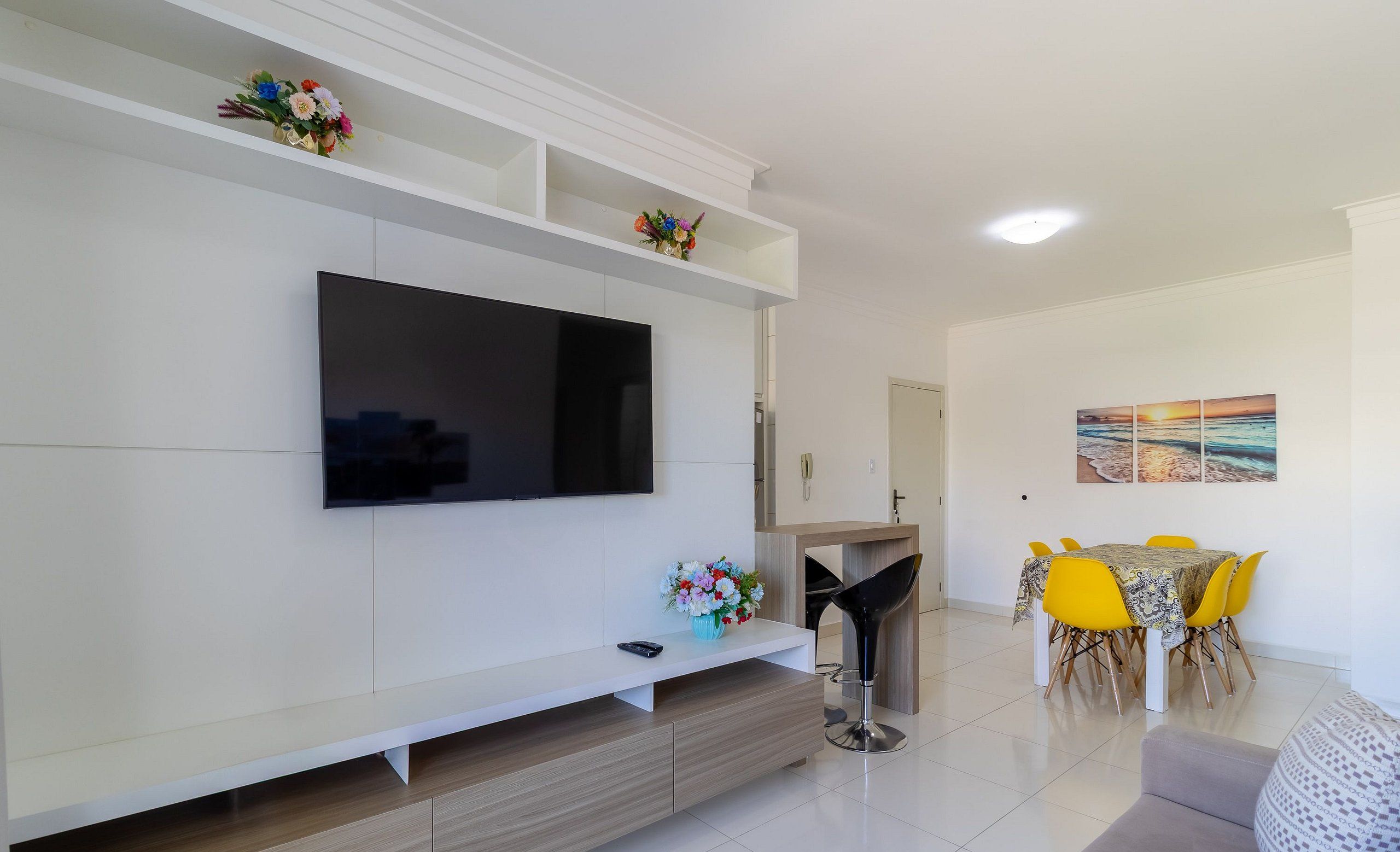Una sala de estar moderna con una televisión de pantalla plana, un comedor con sillas amarillas y un sofá.