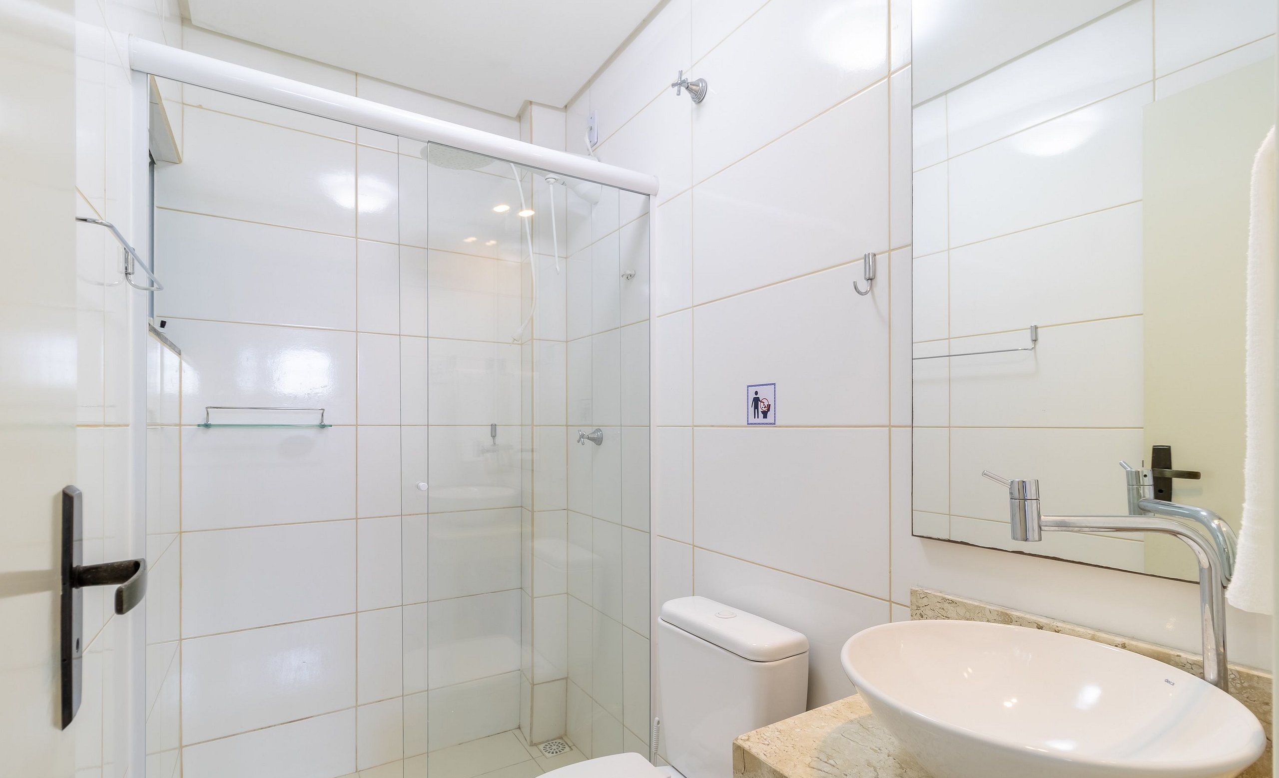 Une salle de bain moderne avec une douche à parois de verre, des toilettes blanches et un grand lavabo ovale surmonté d’un miroir.