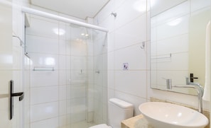 Een moderne badkamer met een douchecabine van glas, een wit toilet en een groot ovaal wastafel met een spiegel erboven.