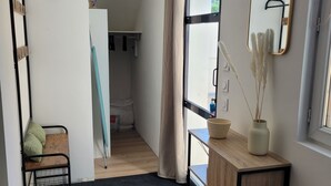 A modern room with a wooden floor, a black metal bench, a small cabinet, a mirror, and a view of a bathroom.