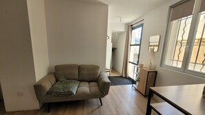 A modern living room with a sofa, a dining table, and a kitchen area visible through an open door.