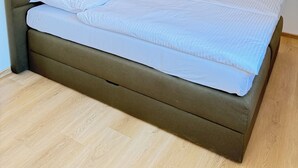 A single bed with a brown headboard in a room with white walls and wooden flooring.