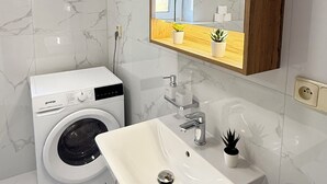 A modern bathroom with a built-in washing machine, a sink with a mirror above it, and a wooden shelf with decorative items.