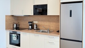 A modern kitchen with white cabinets, a stainless steel refrigerator, a built-in oven, a microwave, and a wooden countertop.