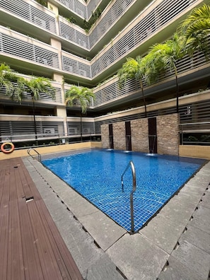 A modern indoor pool with a wooden deck and stone walls, surrounded by multi-level balconies with greenery.