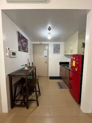 A compact kitchen with a dining table, chairs, a red refrigerator, and a microwave.