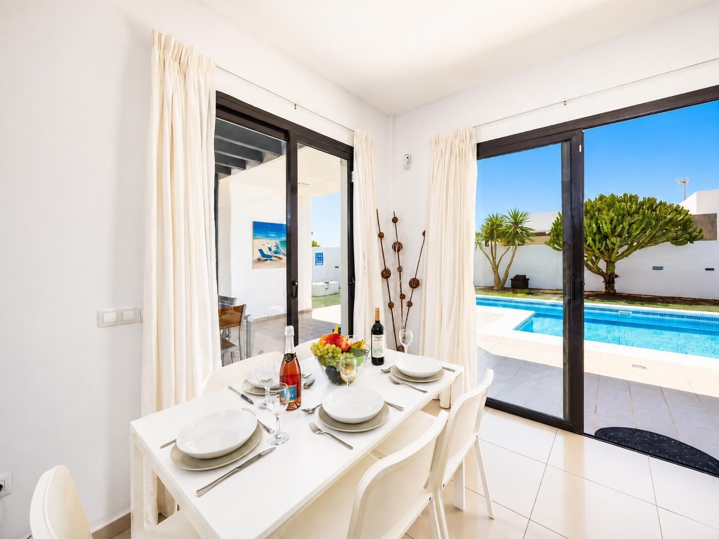 A dining area with a table set for four, a pool visible through the glass doors, and a view of the poolside area.