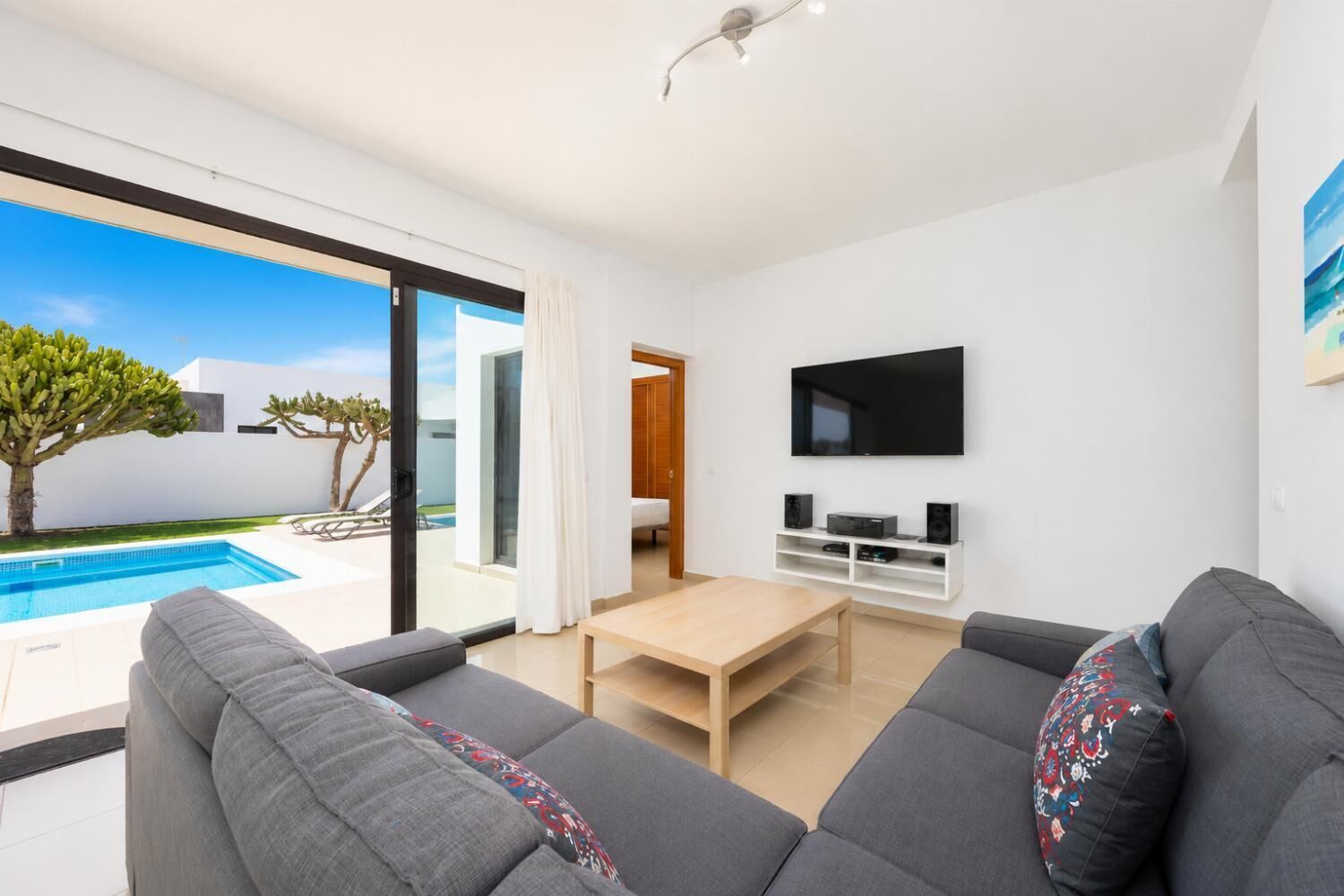 Een moderne woonkamer met uitzicht op een zwembad, een flatscreen-tv en een minimalistisch design.