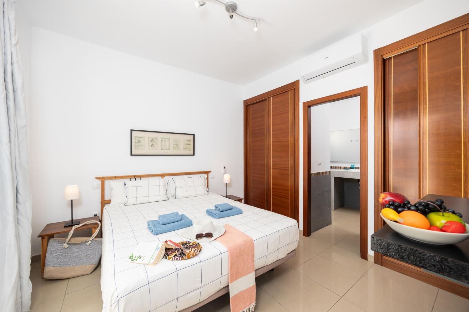 Une chambre d’hôtel comprenant un lit, des tables de chevet, un panier de fruits et une armoire.