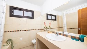 A bathroom with a white sink, a mirror, a toilet, and a window above the sink.